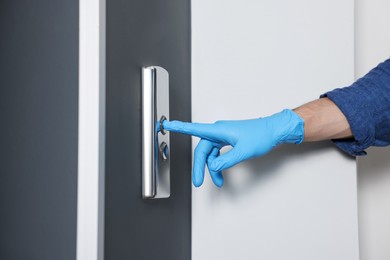 Photo of Man in glove pressing elevator call button, closeup. Protective measure