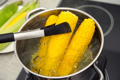 Photo of Taking boiled corn from pot with tongs in kitchen, closeup