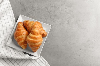 Plate with tasty croissants and space for text on grey background, top view. French pastry