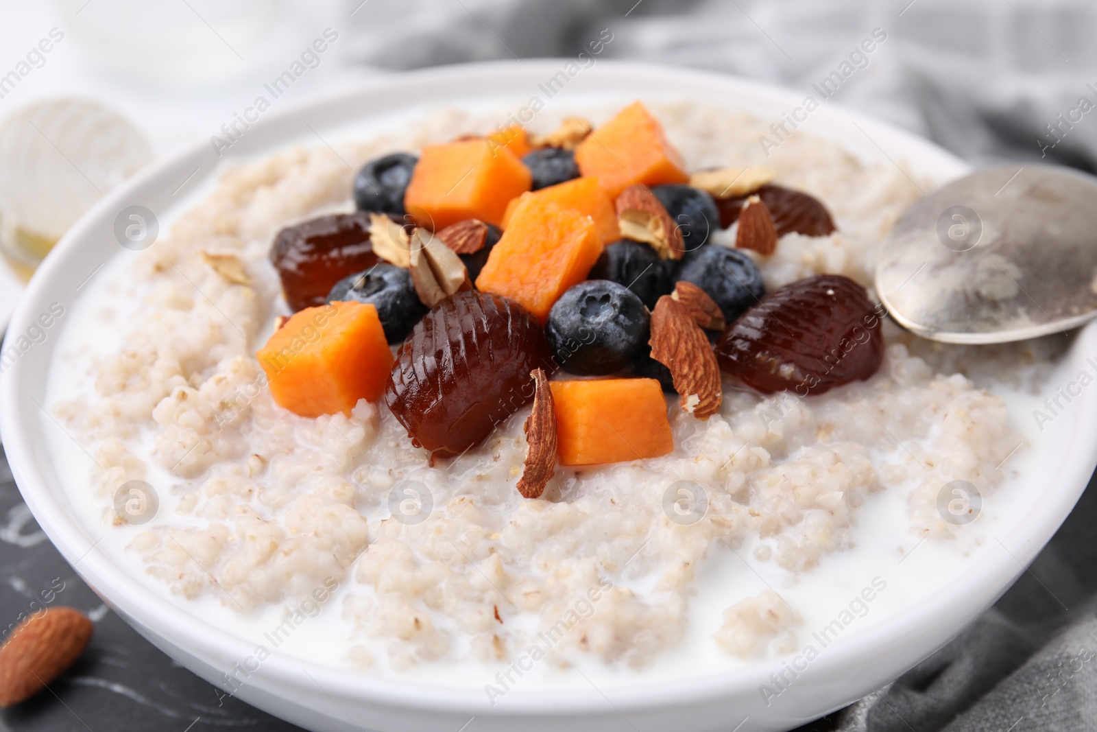 Photo of Delicious barley porridge with blueberries, pumpkin, dates and almonds in bowl on table, closeup