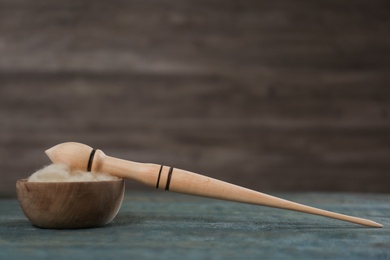 Photo of Soft white wool and spindle on blue wooden table. Space for text