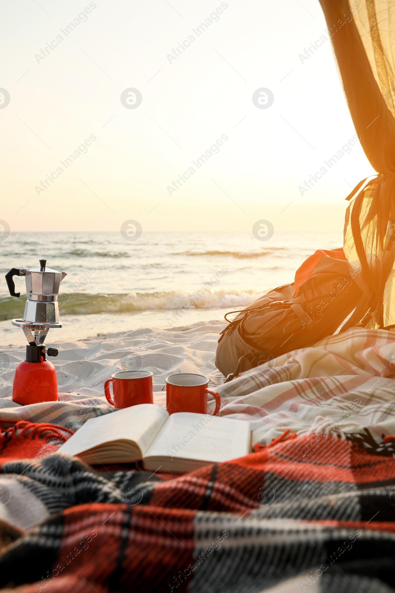 Photo of Cups, book on blanket and backpack in camping tent. View from inside