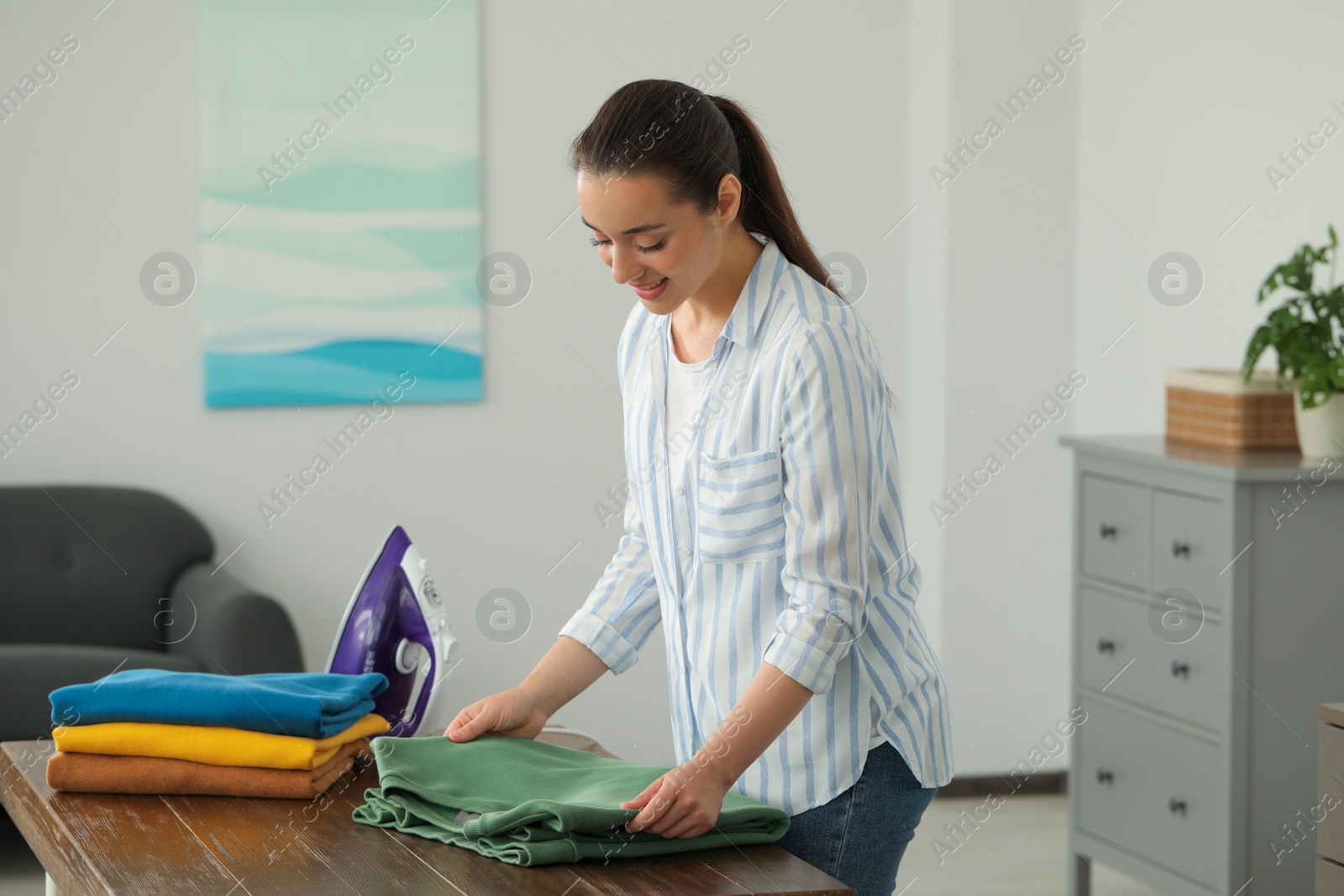 Photo of Young woman folding clothes at wooden table indoors