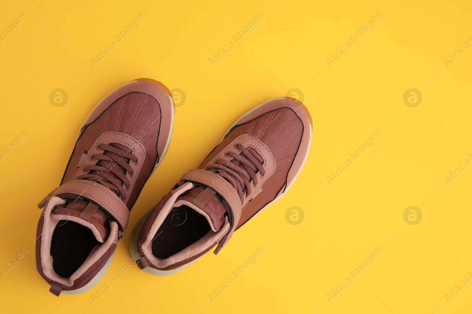 Photo of Pair of stylish kid's sneakers on yellow background, top view. Space for text