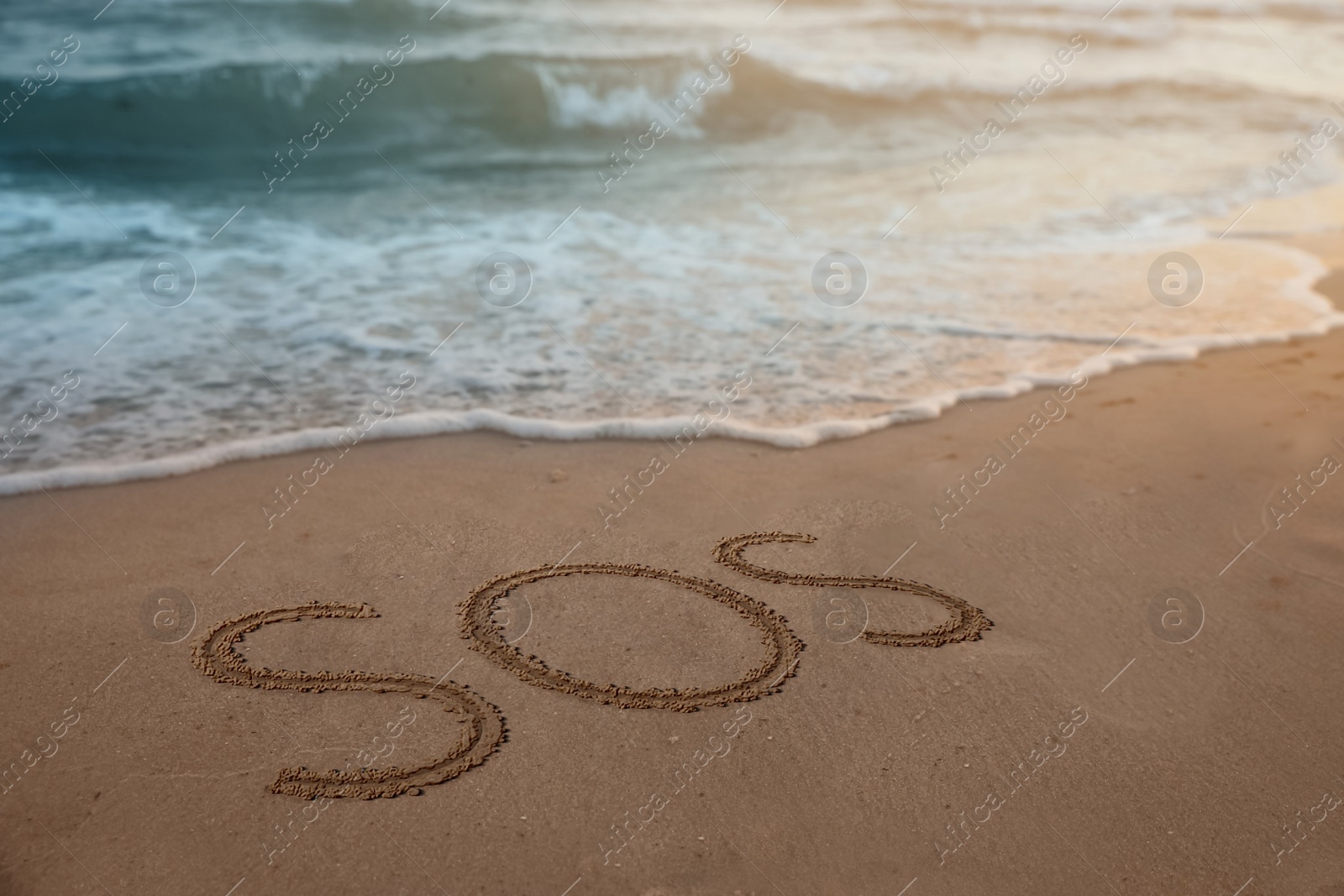 Image of SOS message drawn on sandy beach near sea