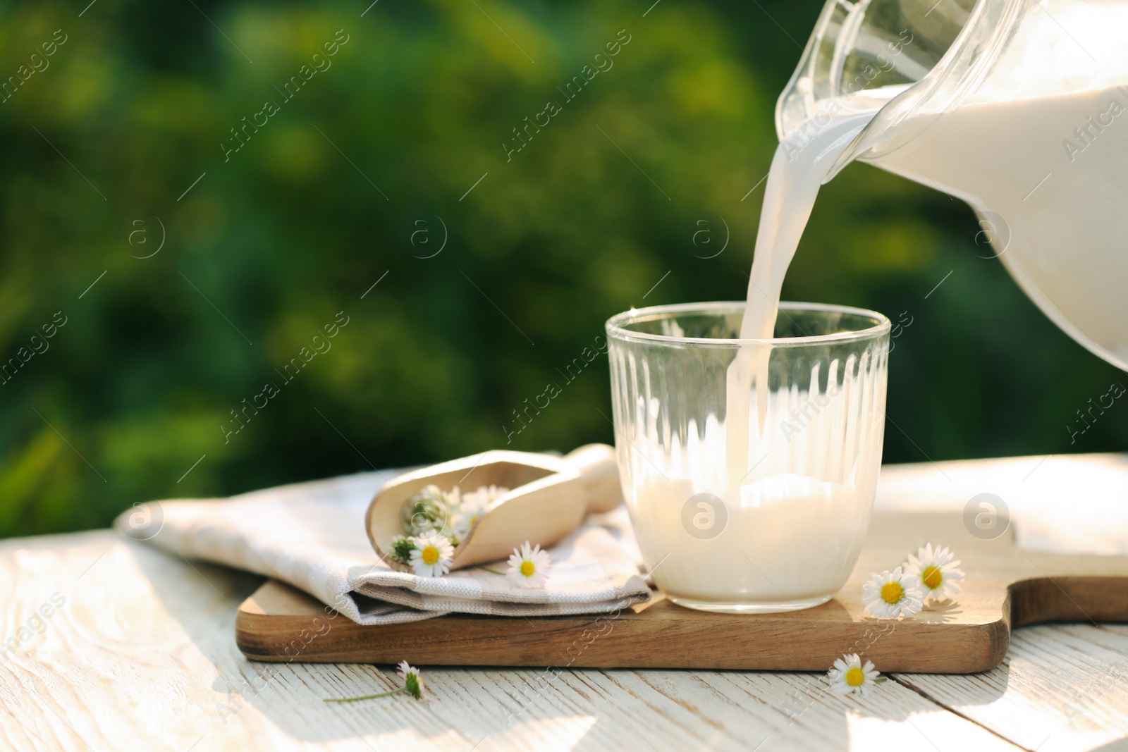Photo of Pouring tasty fresh milk from jug into glass on white wooden table, closeup. Space for text
