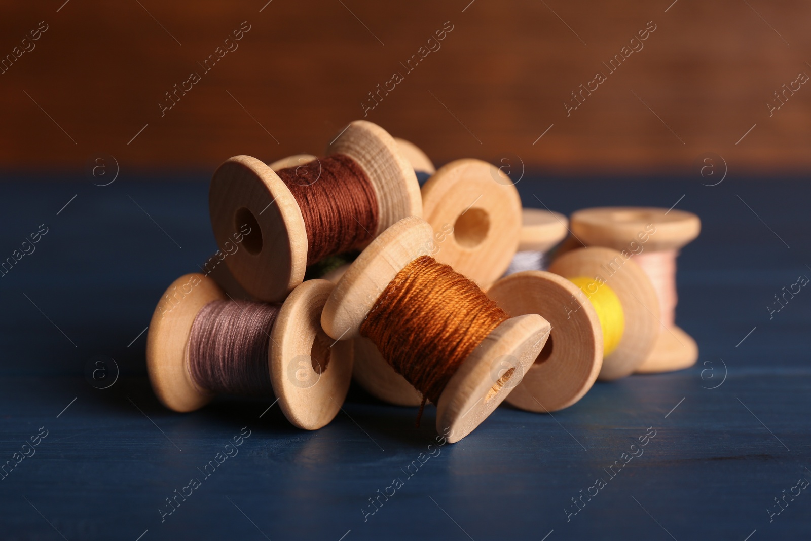 Photo of Set of color sewing threads on blue wooden table, closeup