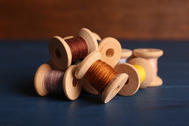 Photo of Set of color sewing threads on blue wooden table, closeup