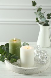 Photo of Burning candles and branches of eucalyptus on white table indoors, space for text