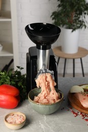 Photo of Electric meat grinder with chicken mince and products on grey marble table indoors