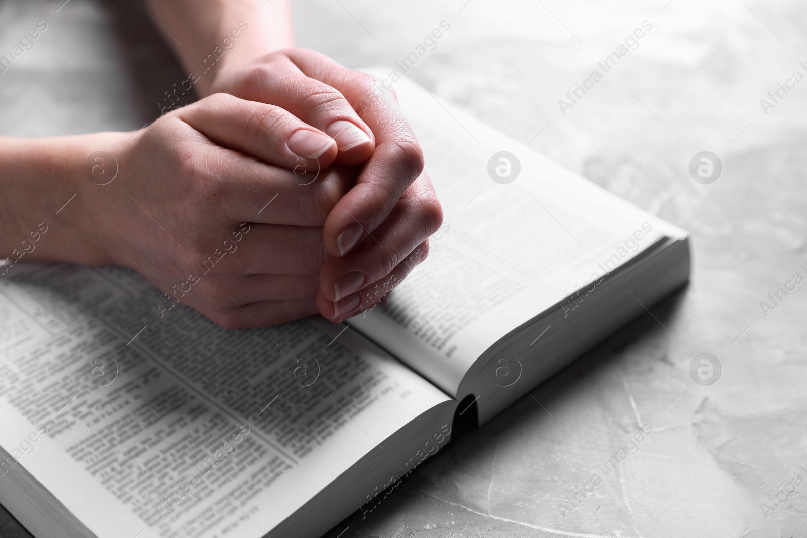 Photo of Religion. Christian woman praying over Bible at gray textured table, closeup