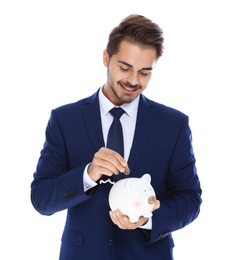 Young businessman putting money into piggy bank on white background