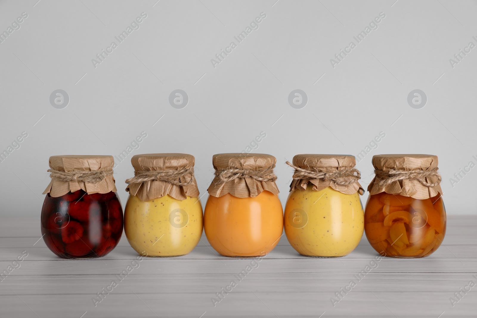 Photo of Jars with preserved fruit jams on white wooden table