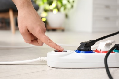 Photo of Woman pressing power button of extension cord on floor indoors, closeup. Electrician's professional equipment