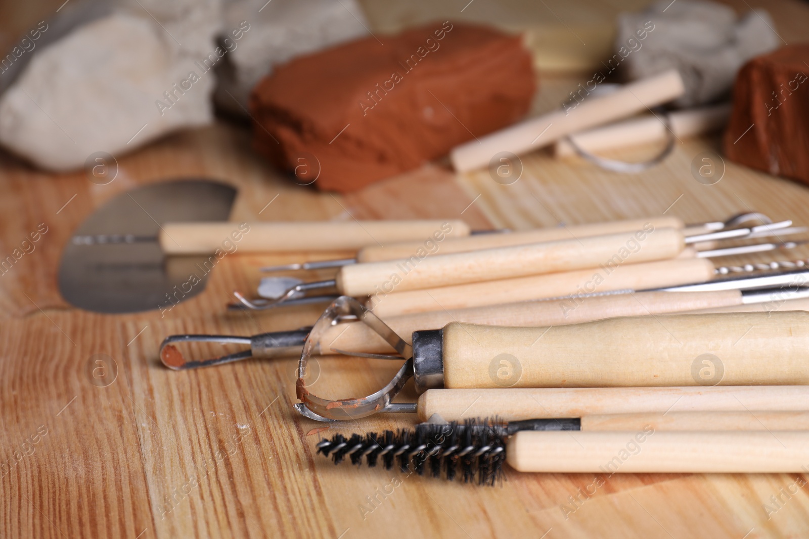 Photo of Clay and set of modeling tools on wooden table, closeup