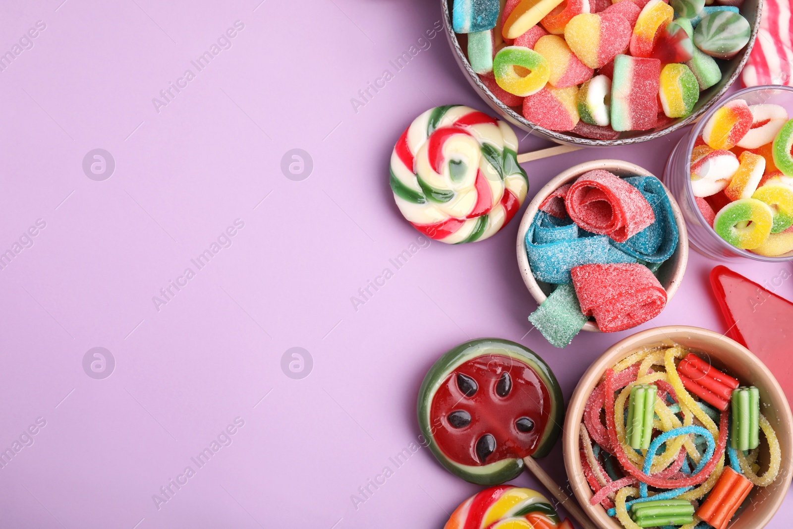 Photo of Many different jelly candies and lollipops on lilac background, flat lay. Space for text