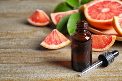 Photo of Citrus essential oil and grapefruits on wooden table. Space for text