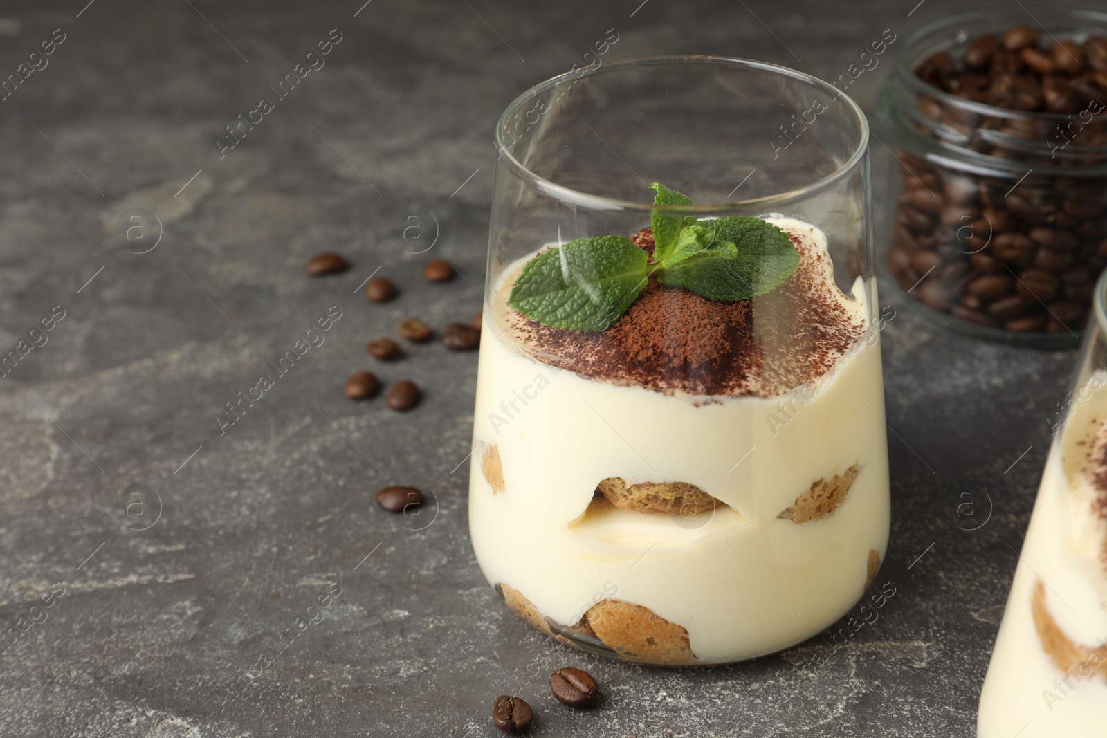 Photo of Delicious tiramisu with mint in glass on grey table. Space for text