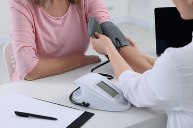 Doctor measuring blood pressure of woman at table indoors, closeup