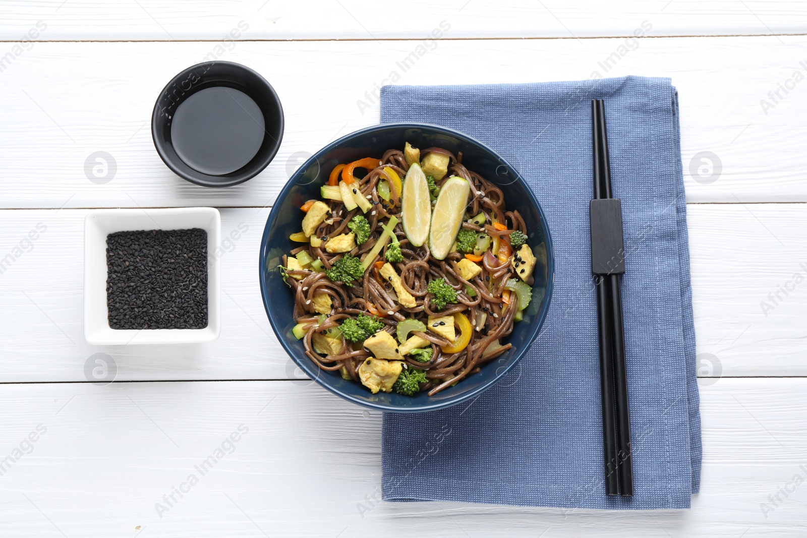 Photo of Stir-fry. Delicious cooked noodles with chicken and vegetables in bowl served on white wooden table, flat lay