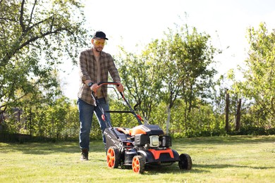 Man cutting green grass with lawn mower in garden