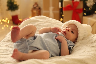 Cute little baby on knitted blanket in room decorated for Christmas