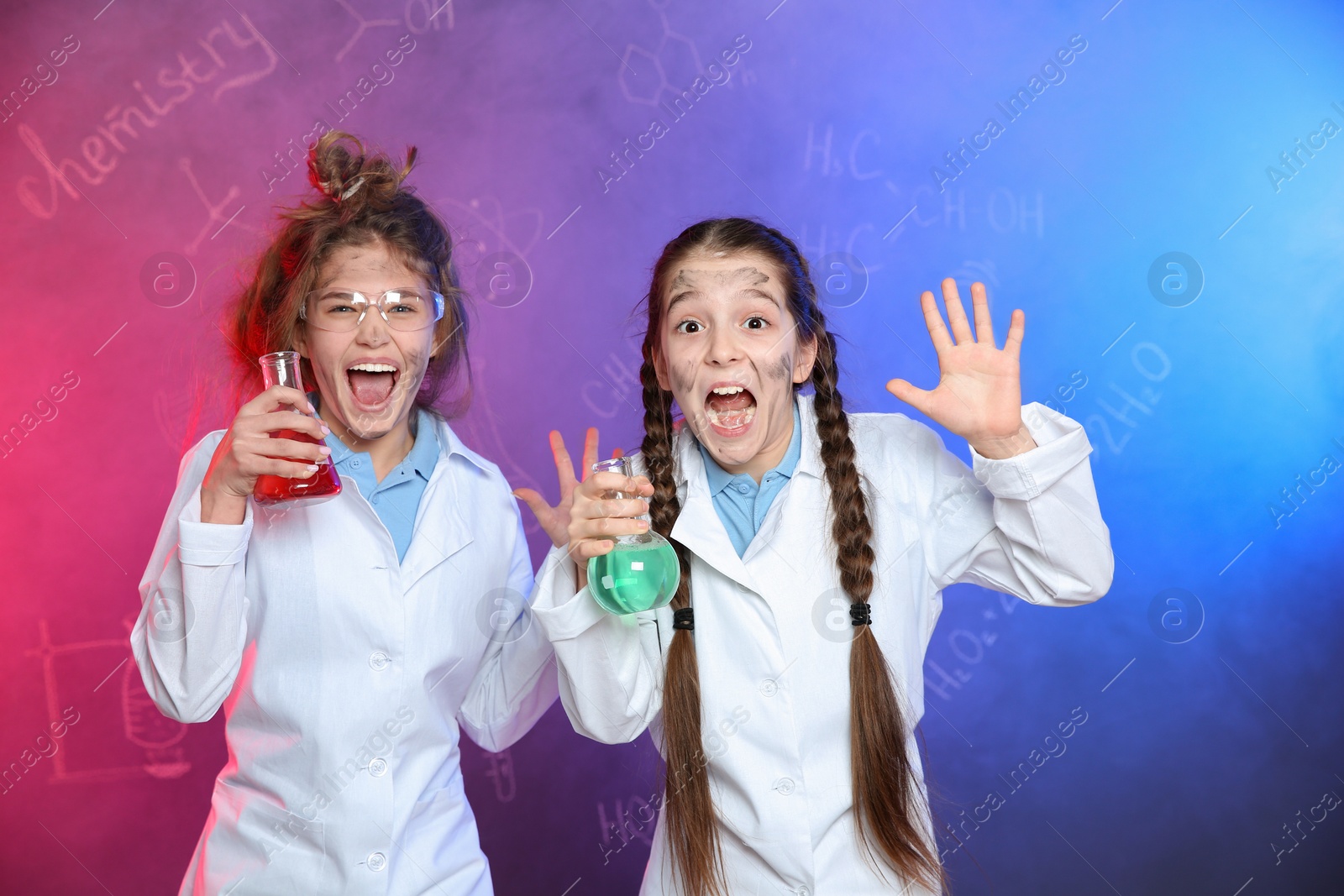 Photo of Emotional pupils holding flasks in smoke against blackboard with chemistry formulas