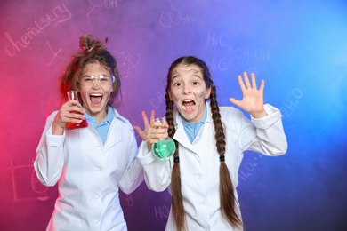 Emotional pupils holding flasks in smoke against blackboard with chemistry formulas