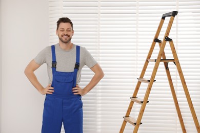 Photo of Worker in uniform and stepladder near horizontal window blinds indoors