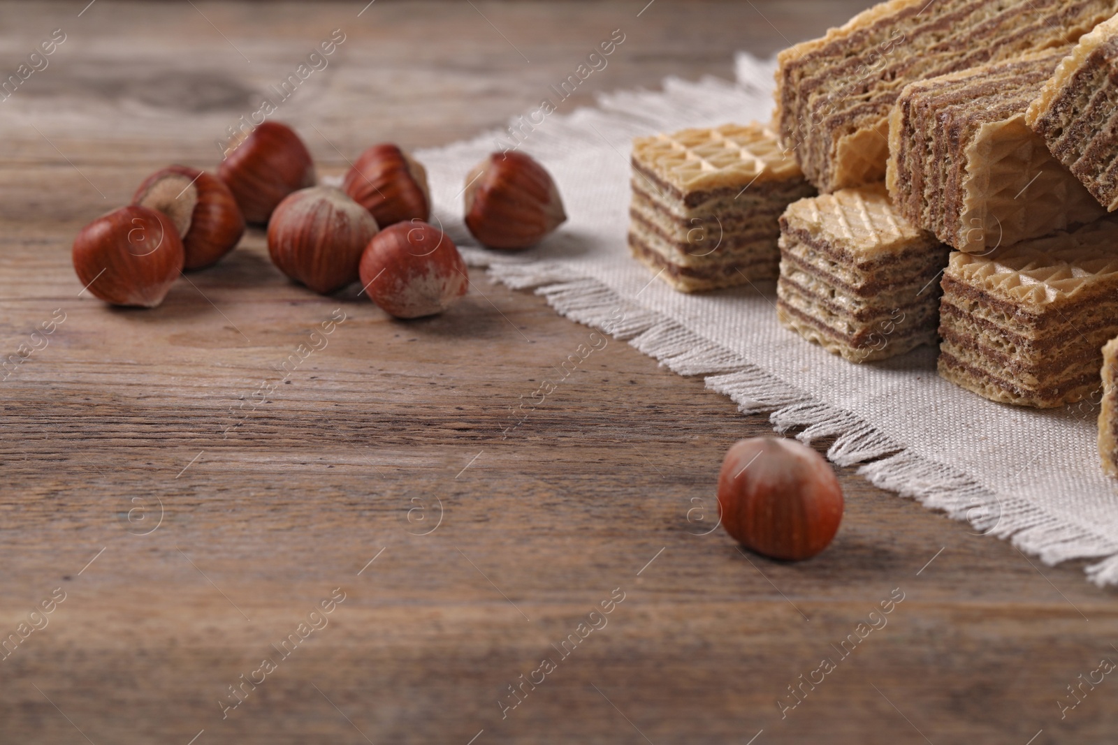 Photo of Delicious wafers with hazelnuts on brown wooden background. Space for text