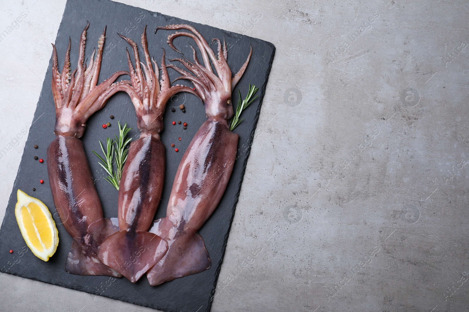 Photo of Fresh raw squids with lemon, rosemary and pepper on grey table, top view. Space for text