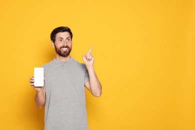 Happy man with smartphone pointing at something on yellow background. Space for text