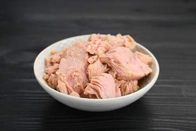 Bowl with canned tuna on black wooden table, closeup