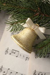 Golden shiny bell with bow, music sheets and fir branches on light table, flat lay. Christmas decoration