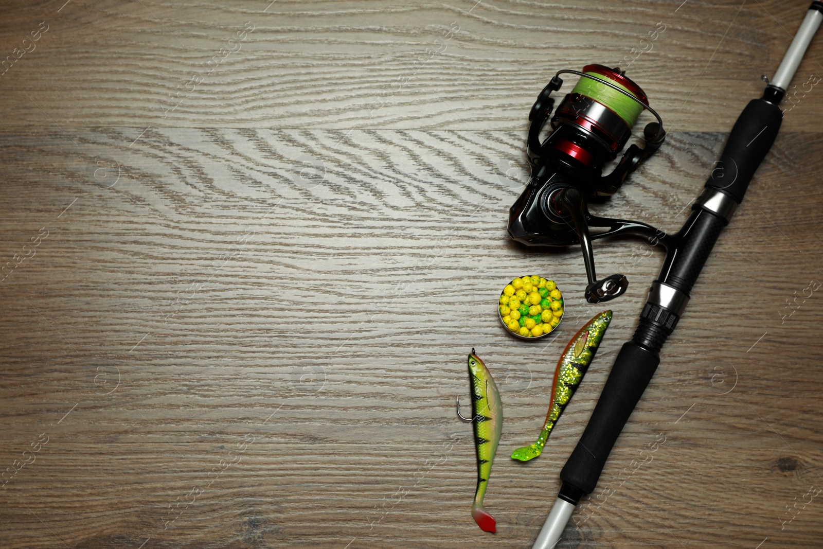 Photo of Fishing rod with spinning reel and baits on wooden background, flat lay. Space for text