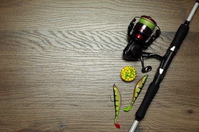 Photo of Fishing rod with spinning reel and baits on wooden background, flat lay. Space for text