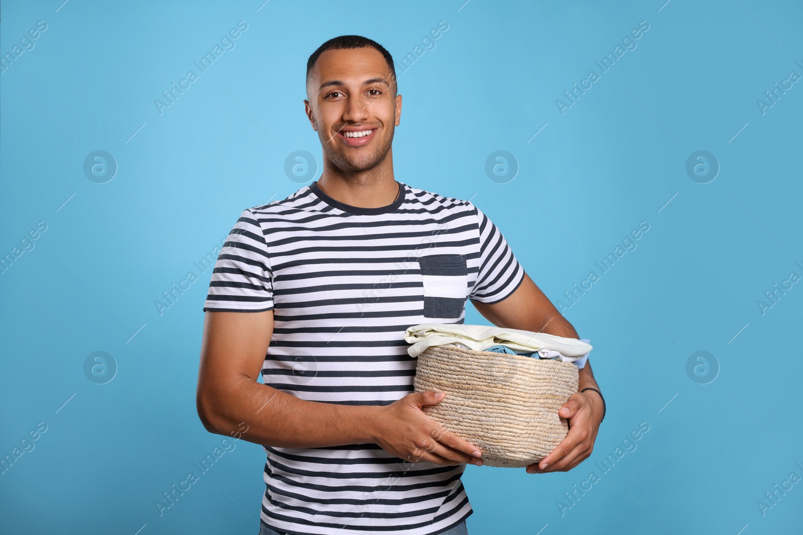 Photo of Happy man with basket full of laundry on light blue background