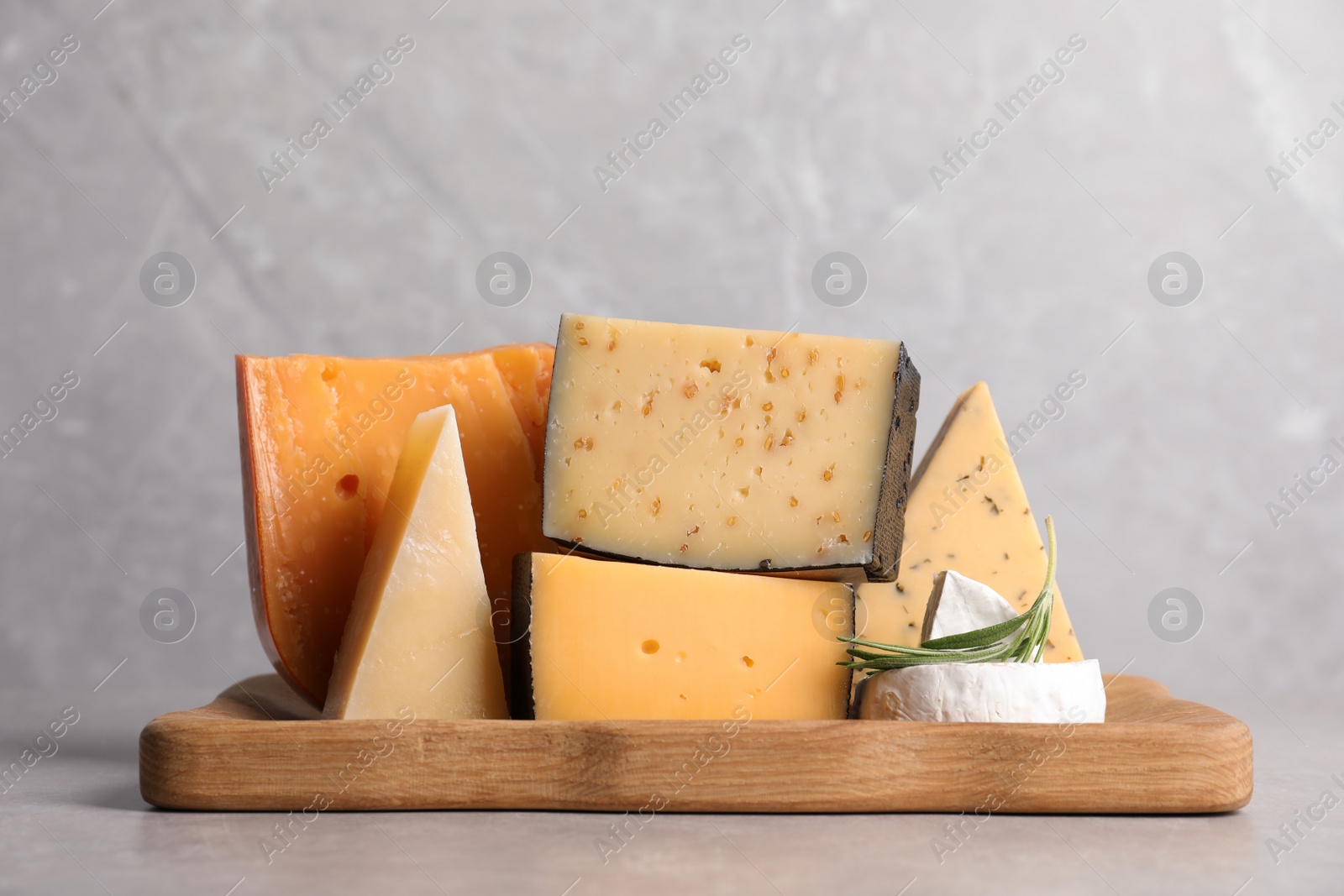 Photo of Wooden tray with different sorts of cheese and rosemary on grey table