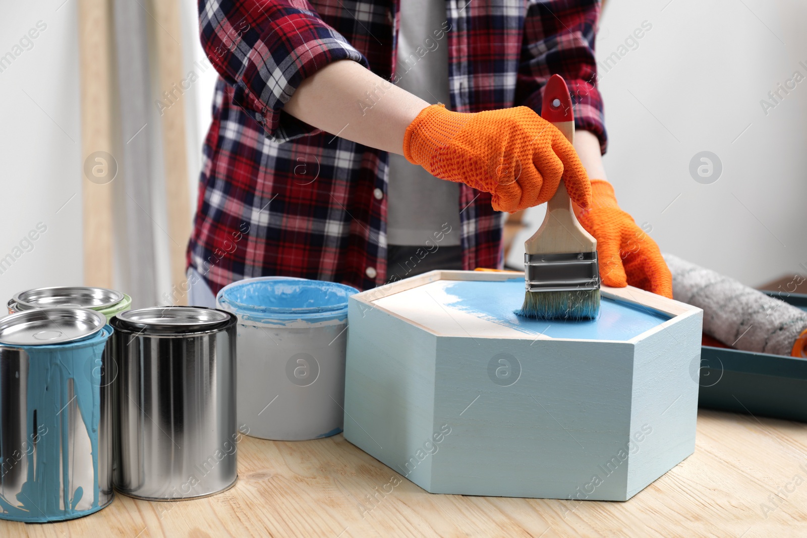 Photo of Woman painting honeycomb shaped shelf with brush at wooden table indoors, closeup