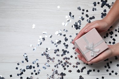 Photo of Christmas present. Woman with gift box and confetti on white wooden background, top view. Space for text