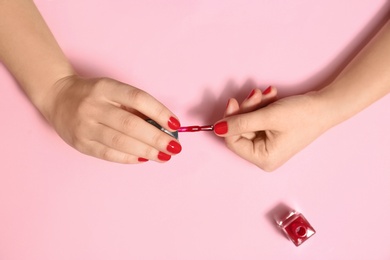 Photo of Woman applying nail polish on color background, top view