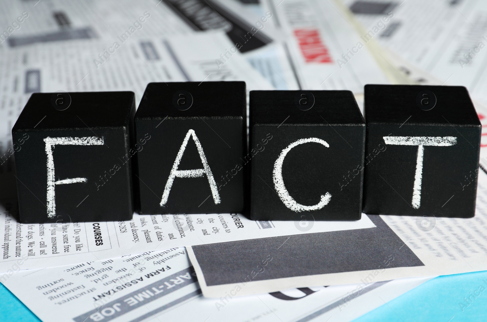 Photo of Word FACT made with black cubes and many newspapers on light blue background, closeup