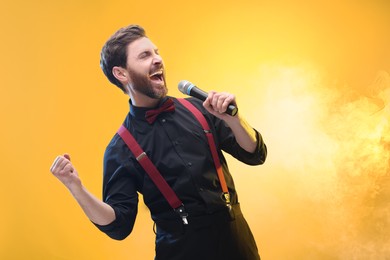 Photo of Emotional man with microphone singing on yellow background. Space for text