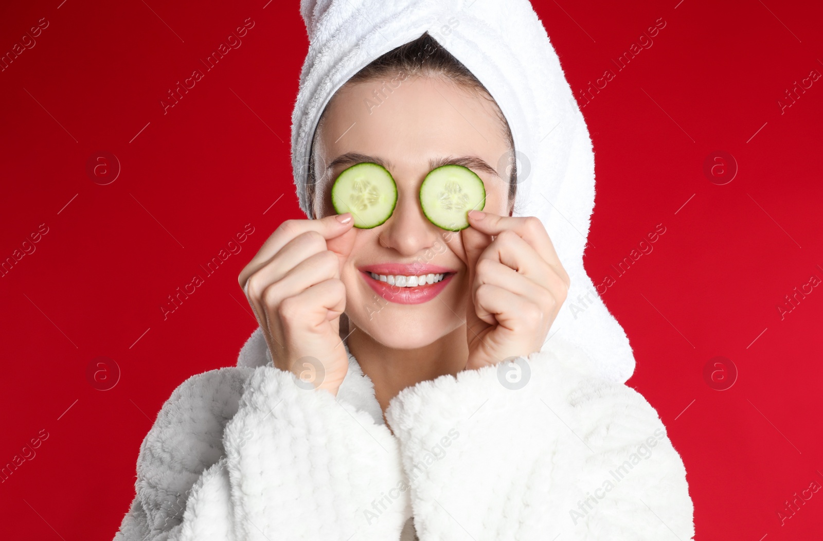 Photo of Young woman in bathrobe with cucumber slices on red background