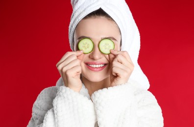 Young woman in bathrobe with cucumber slices on red background