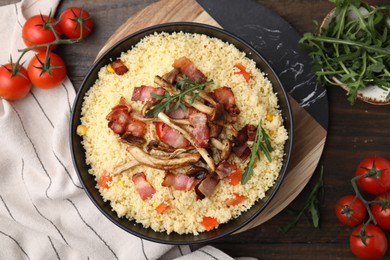 Photo of Bowl of tasty couscous with mushrooms, bacon and tomatoes on wooden table, flat lay