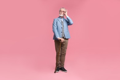 Senior man with walking cane on pink background