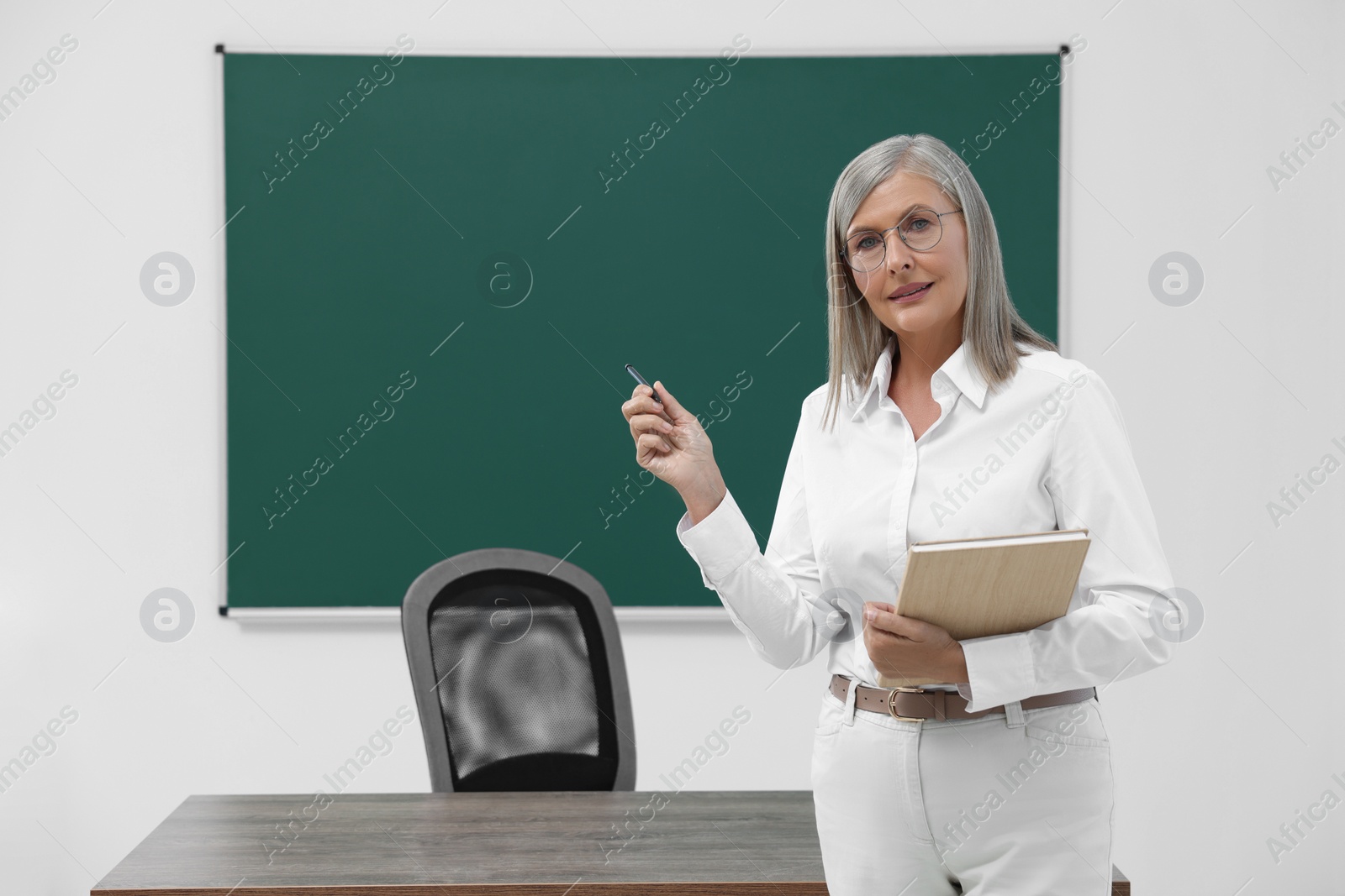 Photo of Portrait of professor with pen and notebook near blackboard in classroom, space for text