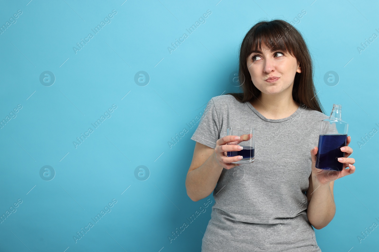 Photo of Young woman using mouthwash on light blue background, space for text