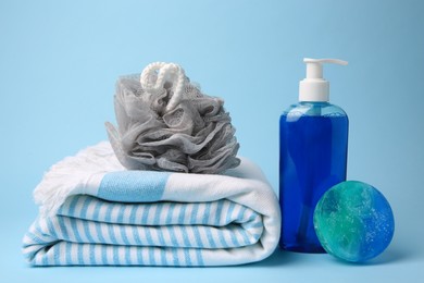 Grey shower puff, cosmetic products and towel on light blue background